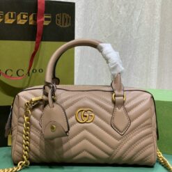 Beige quilted handbag with gold GG logo, chain strap, displayed in front of a Gucci shopping bag.