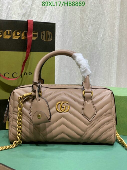 Beige quilted handbag with gold GG logo, chain strap, displayed in front of a Gucci shopping bag.