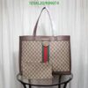 Large brown designer tote bag with matching pouch on glass table, white curtain background.